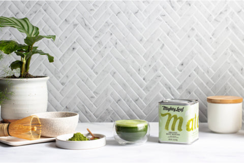 A countertop with a tin of Mighty Leaf Organic Mint Matcha, as well as a cup of Organic MInt Matcha and a matcha whisk.